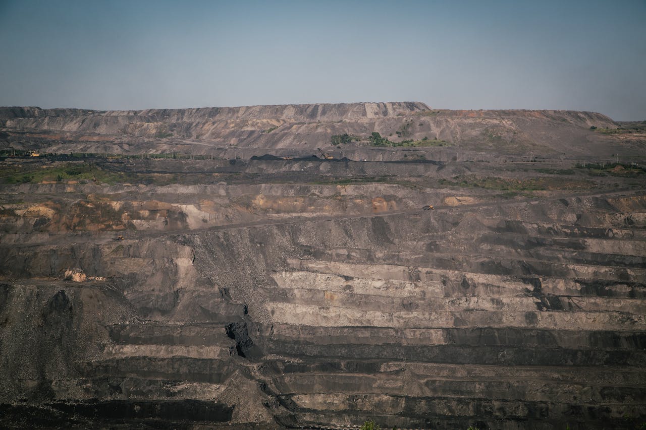 A vast open-pit coal mine under a clear blue sky, showcasing industrial landscape and natural rock formations.